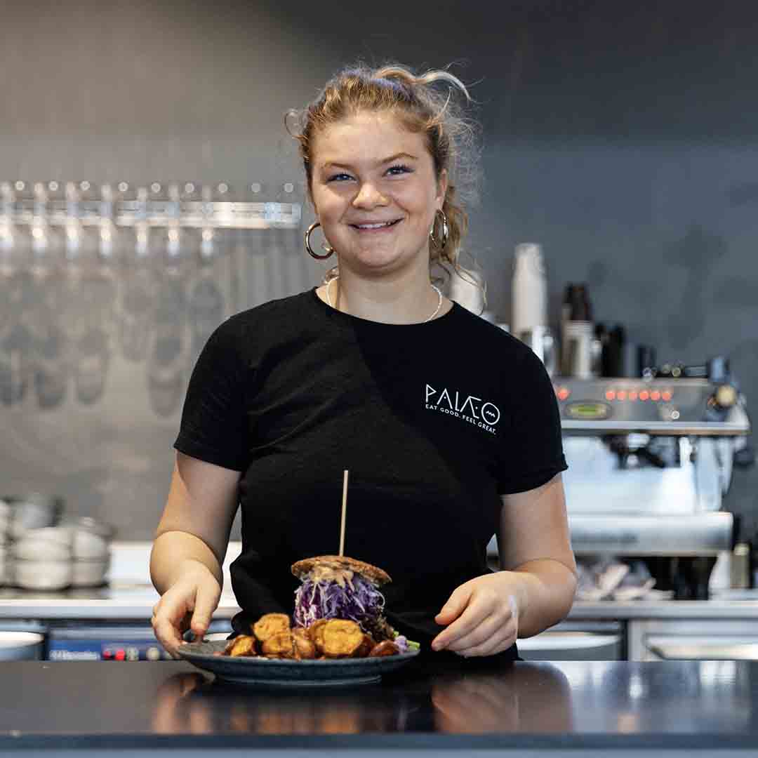 Smiling employee from Palæo in Frederiksberg Center holding food.